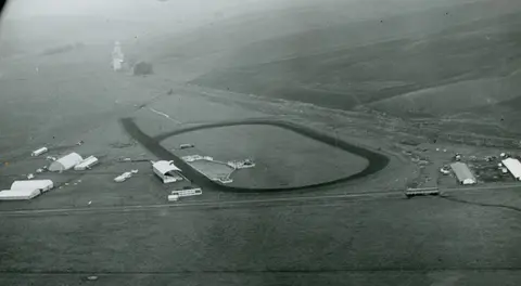 An aerial view of a racetrack and surrounding buildings in a rural landscape.