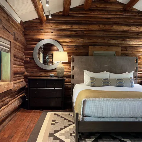 A rustic bedroom with log walls, a bed, a dresser, and a round mirror.