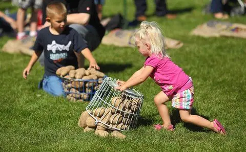 Two children play with baskets filled with potatoes on a grassy lawn.