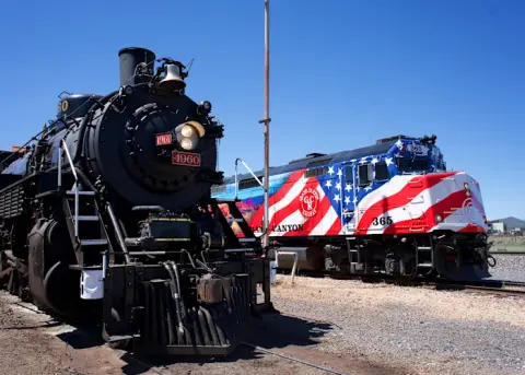 A steam locomotive and a diesel locomotive parked on train tracks under a blue sky.