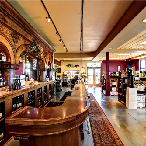 An interior view of a store with a long wooden bar and shelves of wine.