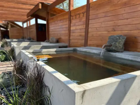 A row of outdoor concrete soaking tubs with wooden walls and overhead structures.