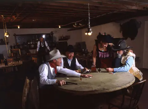 People dressed in period western attire playing cards in a saloon.