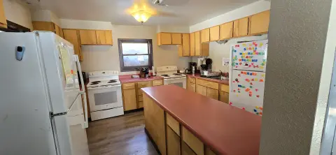 A view of the interior kitchen with wooden cabinets and white appliances.