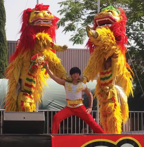 A performer posing between two lion dance costumes outdoors.