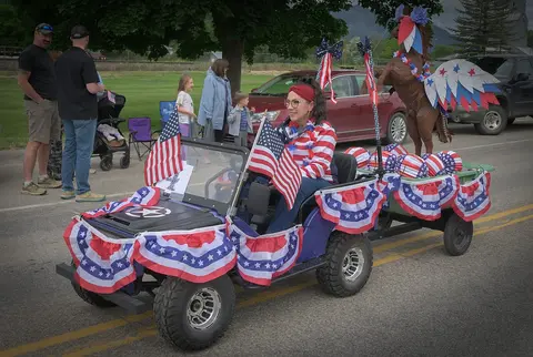 A woman drives a patriotic-themed decorated golf cart in a parade.