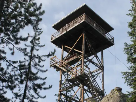 A tall wooden fire lookout tower stands among trees.