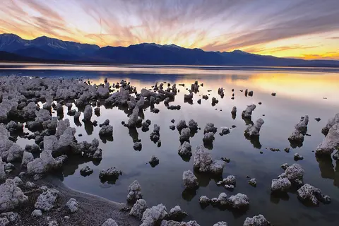 A sunset over a lake with tufa rock formations in the water.