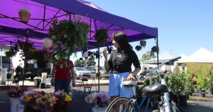 A woman stands near a bicycle at an outdoor market under purple tents.