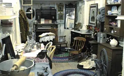 An interior view of a historic room filled with antique furnishings and household items.