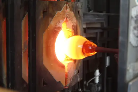 A glowing molten glass piece is heated inside a kiln.