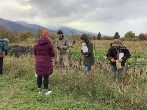 A group of people gathered in an outdoor field with mountains in the background.