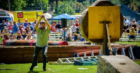 A man throws an axe at a wooden target while spectators watch.