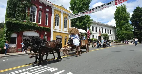 A horse-drawn wagon travels down a street lined with historic buildings during an event.