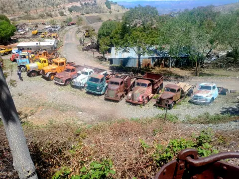 A collection of old, rusty vintage trucks parked in a rural, hilly landscape.