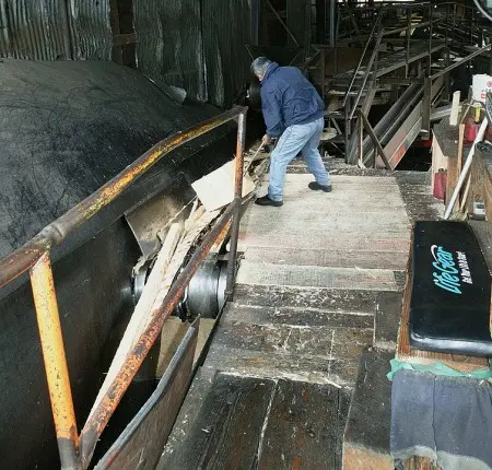 A person working inside an industrial facility with conveyors and wood pieces.