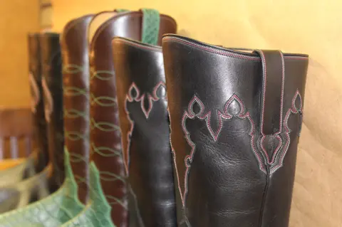 A row of leather cowboy boots lines up against a wall.