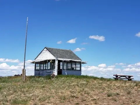 A small white building sits on a grassy hill under a blue sky.