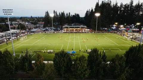 An elevated view of a soccer match being played on a lighted field at dusk.
