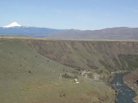 An aerial view of a landscape with hills, a river, and a snow-capped mountain in the distance.