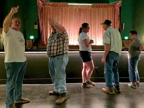 People stand inside a room with a stage and a curtain in the background.