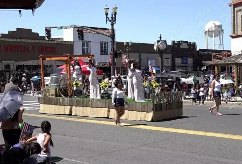 People and a parade float move down a street lined with buildings.