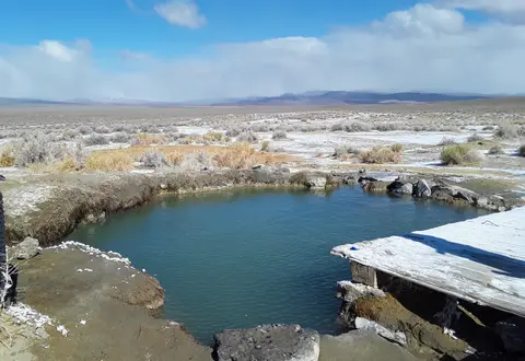 A natural hot spring pool in a desert landscape with snow on the ground.