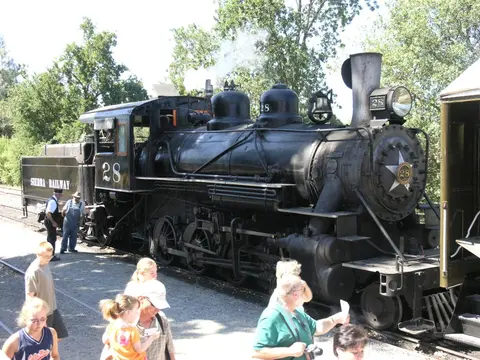 A steam locomotive stands on tracks with people nearby.