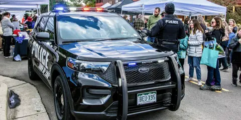 A police SUV parked at an outdoor event with people standing nearby.