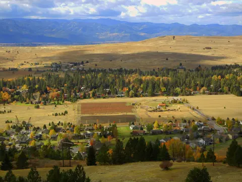 An elevated view of a valley with houses, trees, and distant mountains.