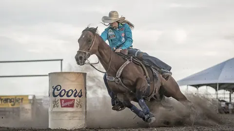 A cowgirl on a horse rounding a barrel during a rodeo.