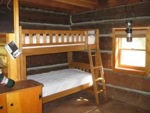 Inside a rustic log cabin bedroom with a wooden bunk bed and a window.