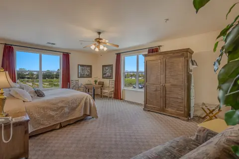 A spacious bedroom with a bed, large wooden wardrobe, and windows looking out onto a landscape.