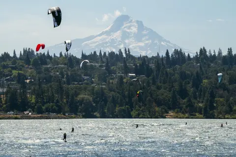 Kiteboarders riding on a river with a snow-capped mountain in the background.