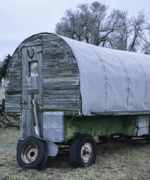 A covered wagon sits outdoors on grass under an overcast sky.
