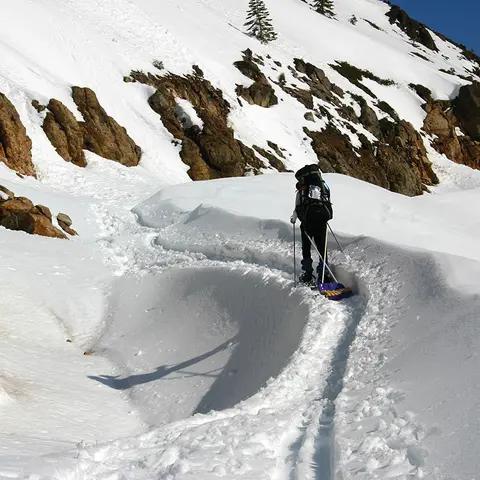 A person hikes on a snow-covered mountain with a backpack and poles.