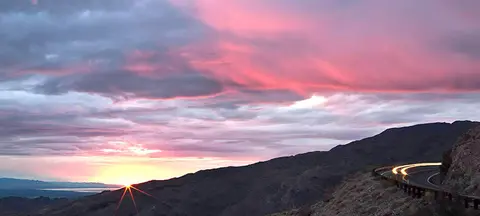 A sunset over hills with a curving road in the foreground.