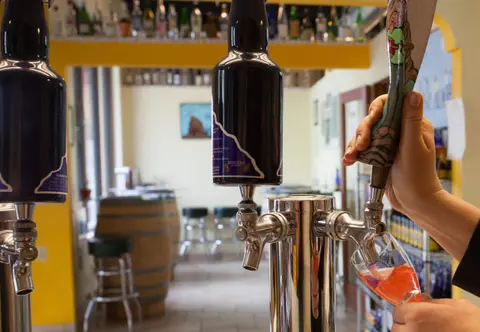 A person pours a beverage from a tap inside a bar.