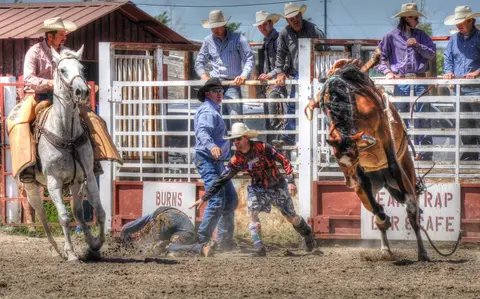 A rodeo event in progress with a bucking horse and a fallen rider.
