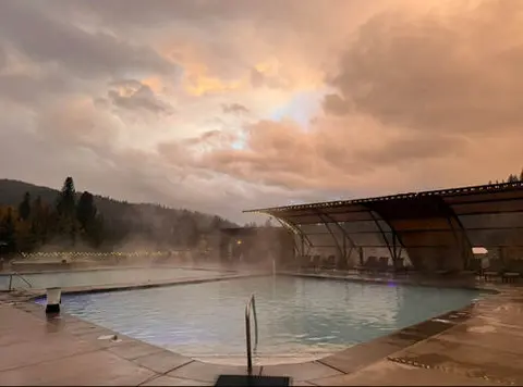 An outdoor hot springs pool under a dramatic cloudy sky at dusk.