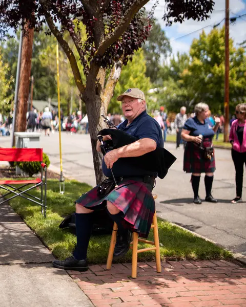 A man playing bagpipes while sitting on a stool outdoors.