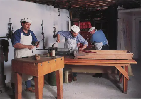 Three butchers working together to make sausage in an interior workshop.
