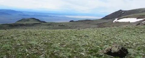 A wide landscape view from a high mountain slope overlooking a valley.