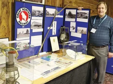A man stands beside a display table with historical photographs and artifacts.