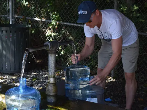 A man fills large plastic water jugs from an outdoor spigot.