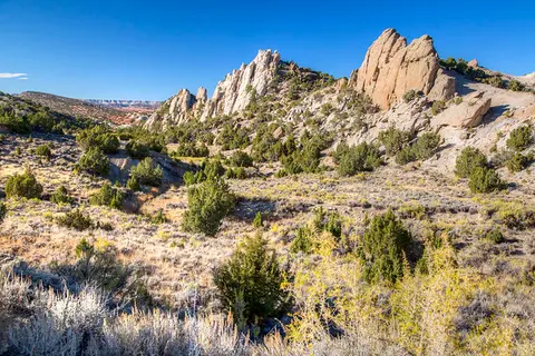 A scenic landscape featuring rocky cliffs and sparse vegetation under a clear blue sky.