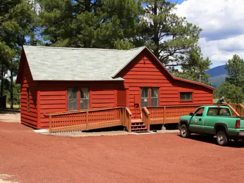 A red wooden building with a ramp and a green pickup truck parked outside.