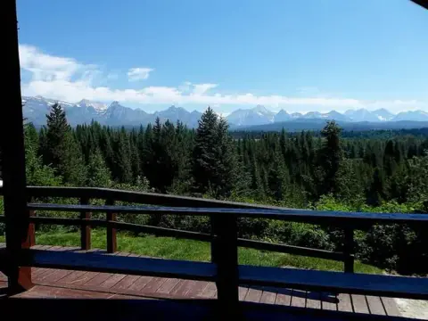 A view of a mountain range and forest from a wooden deck.