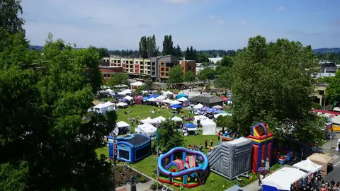 High-angle view of an outdoor community event with tents and bouncy houses in a park.