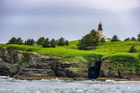 A lighthouse stands on a grassy cliff overlooking the ocean.